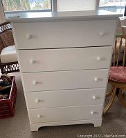 Front view of the white dresser showing all five drawers closed with white round knobs.