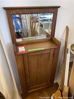 Front view of the wooden wall cabinet with mounted mirror on top and closed wooden door below.