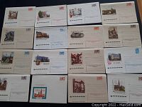 Full view of 16 vintage prepaid stamped envelopes arranged in rows, showing artwork and printed stamps on each