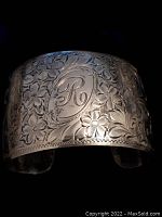 Close-up photo of the front of the bangle showing detailed floral engraving and monogrammed letter 'R' in the center.