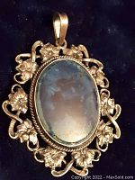 Front view of antique sterling silver pendant with dark blue polished agate stone and detailed flowered silver border