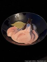 Image showing front top view of small round plate with stylized pink flower relief design on dark glossy background.