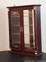 Front angled view of small wood and glass curio cabinet highlighting decorative gold accents and etched designs on glass doors.