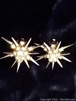 Front angle view of both clip-on earrings showing starburst design with rhinestones and spikes.