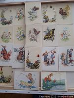 Photo showing the complete layout of 18 vintage postcards with butterflies and children illustrations spread out for display, showing variety of scenes with floral and playful child imagery.