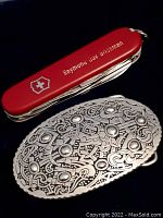 Red Swiss Army pocket tool with white logo and monogram alongside medieval style belt buckle.
