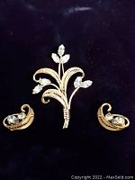 Top view of the brooch and earrings set showing the floral design of the brooch and the curved matching earrings with aquamarine stones