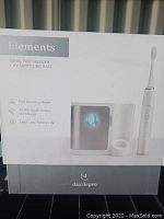 Front view of the product box showing the Elements Sonic Toothbrush with UV sanitizing base, listing features like four brushing modes, 40,000 brush strokes per minute, and extra-long battery life.