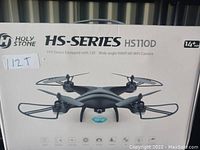Photo showing the Holy Stone HS-Series HS110D drone in its retail packaging. Displays image of drone, branding and key features including the camera angle and resolution, and suitable age indication.