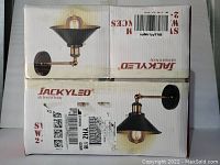 Box showing Jackyled logo, sub-brand Aracky, and image of a single swing arm wall sconce with black shade and brass arm and round black wall mount.