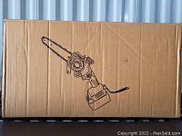 Cardboard box with black line drawing of a 6 inch mini chainsaw on front, box unopened and sealed.