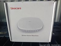 Box front showing Sinocare white noise machine, white, shell style design with control buttons on front.