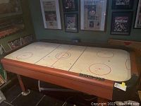 Air hockey table from above showing full playing surface with scratches and black pucks lined along the edges.