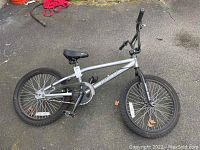 Side view of entire silver bike leaning on pavement