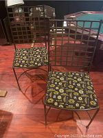 Photo showing two metal chairs with grid style backs and Boston Bruins printed fabric seat cushions, placed on hardwood floor near a pool table.