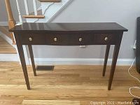 Front view of the dark wood console table showing three drawers and brass knobs.