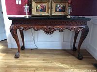 Front view of wood console table with carved apron and claw feet, topped with a dark stone-like surface.