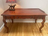 Front view of wooden desk showing three drawers with round knobs and curved legs on polished wood floor.