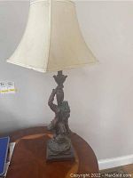 Full view of the lamp showing the square fabric shade and monkey figure base on wooden surface.