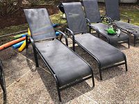 Two black mesh outdoor lounge chairs placed on a patio, showing the full length and construction of the chairs.