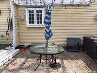 Full view of round patio table with closed umbrella and base on pebbled patio