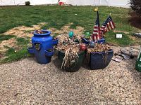 Group of five ceramic garden planters arranged outside on a concrete patio near grass, showing two matching green round planters, two dark blue rectangular planters with glass orbs and flags, and one singular bright blue planter with emblem and small side holders.