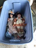 Blue plastic tote containing multiple porcelain dolls with visible detailed vintage-style clothing.