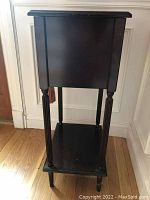 Side view of dark wood side table showing turned legs and bottom shelf