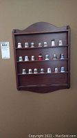 Image showing entire wooden display shelf mounted on wall with 21 thimbles arranged across three shelves.