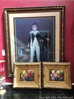 Full view of the three framed paintings: one large portrait and two small floral paintings, displayed against red wallpaper.