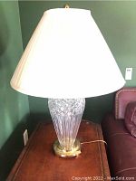 Full view of Waterford crystal table lamp with white pleated shade on wooden table