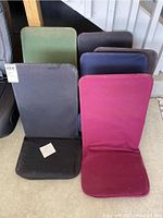 Six canvas bleacher seat and backrest cushions in various colors stacked together, including black, burgundy, green, blue, and purple.