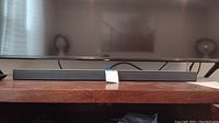 Bose soundbar placed on a wooden shelf beneath a TV, showing the front side of the soundbar with a clean setup.