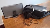 Bose iPod speaker dock, Sennheiser headphones, and the headphones carrying case displayed on a wooden surface.