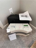 View of Bose Acoustic Wave System along with two user manuals and black soft carrying case. System plugged into wall outlet.