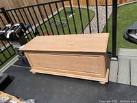 Full side view of the veneered wood storage chest on a deck, showing overall shape and surface.