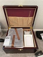 Open wooden box showing burgundy Neptune-planning binder and fabric-wrapped urn with brown strap inside compartments