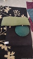 Four pillows arranged showing two black rectangular zabutons, one round green weighted zafu, and one long olive green pillow