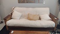 Full front view of futon showing white bamboo patterned mattress cover, three cushions, and wooden frame with wicker sides.