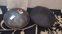 Handpan drum face showing tone fields with two mallets resting on top and case beside it