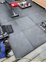 Photo showing three black interlocking cushion floor mat pieces laid on floor with some gym equipment around.