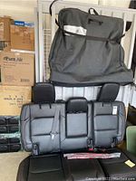 Full view of black Jeep Wrangler rear seat with red stitching, three seats, headrests, and seat belts visible, leaning against garage wall with surrounding boxes.