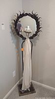 Full standing mirror with metal frame and lotus candleholder seen hanging white scarf.