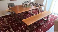 Full view of rectangular wood topped dining table with metal base and two benches on red floral rug