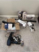 Full view of lot including two boxed Enviro Premium Shower Filters, two boxed Rollize Smart Handheld Eye Massagers, Philips shaver box, black and silver hairdryers, white travel steamer with cords, on carpeted floor.