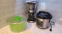 All three items together on countertop: Aroma rice cooker, Oxo salad spinner, and Cuisinart coffee maker