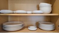 Shelf with stacked white ceramic plates and bowls showing quantity and size variety