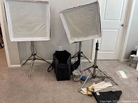 Two softboxes mounted on metal tripods, carrying case, halogen lamps and accessories on floor.