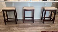 Full view of set of three padded counter height stools lined up at counter