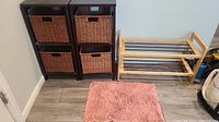 Front view of the two dark wood storage cubes each holding two woven baskets, wooden shoe rack to the right, and small pink throw rug on the floor.
